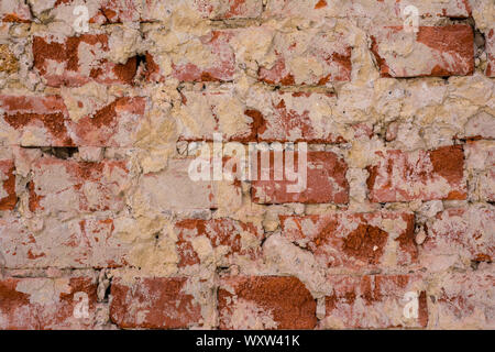 Wall of red crumbling brick, covered with white stucco, background. Stock Photo