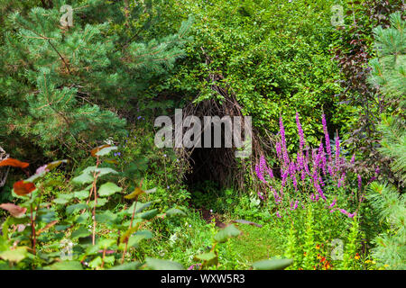 A hut made of dry branches in a picturesque place in forest among green trees and a plants for overnight accommodation away from civilization and peop Stock Photo