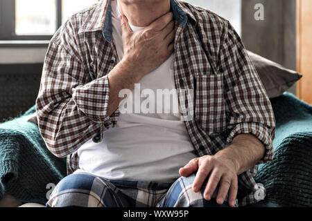 Senior man with throat pain sitting on sofa. No face concept Stock Photo