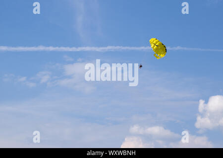 Two people are flying on a yellow parachute towed by the rope against the blue sky. Holiday sport activity. Stock Photo