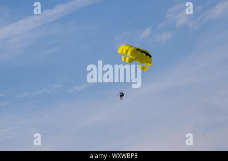 Two people are flying on a yellow parachute towed by the rope against the blue sky. Holiday sport activity. Stock Photo