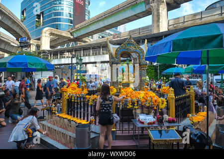 Worshippers at Erawan Shrine in Bangkok, Thailand, praying to a four-faced statue of Hindu god Brahma; above: the BTS rail track & an elevated walkway Stock Photo