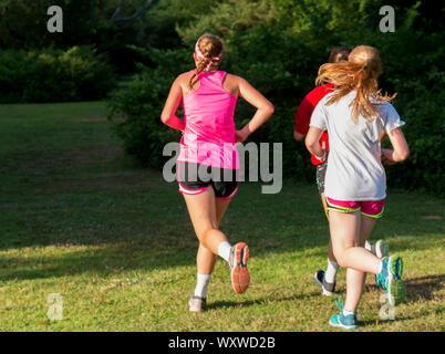 Three girls running together in a park with bright sunlight shining on their backs as the run away from the cameras view. Stock Photo