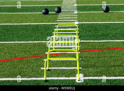 A turf field is set up with six yellow mini hurdles and three medicine balls for strength, agility and speed practice. Stock Photo