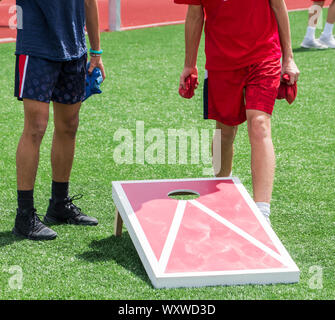Two boys play corn hole during gym class on a green turf field in the sunshine. Stock Photo