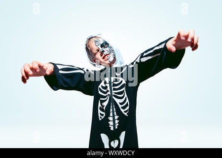 Little boy like a vampire in scary black costume with bones on white background. Caucasian male model looks scary. Halloween, black friday, sales, autumn holidays concept. The night of fear. Stock Photo