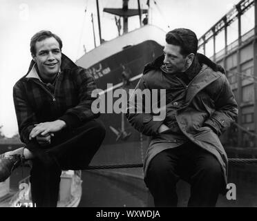 MARLON BRANDO with his stand-in CARL FIORE on set location candid filming ON THE WATERFRONT 1954 director ELIA KAZAN original story / screenplay Budd Schulberg producer Sam Spiegel Horizon Pictures / Columbia Pictures Stock Photo