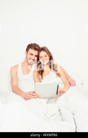 Happy couple in love sitting in bed and looking into tablet Stock Photo