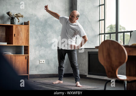 Senior hispanic man practicing yoga trikonasana pose at the living room Stock Photo