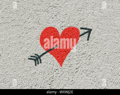 Red heart made like spray paint graffiti on a rough white washed wall. Stock Photo