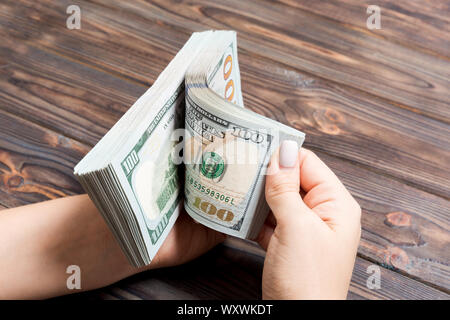 Perspective view of a businesswoman's hands counting one hundred dollar banknotes on wooden background. Success and wealth concept. Stock Photo