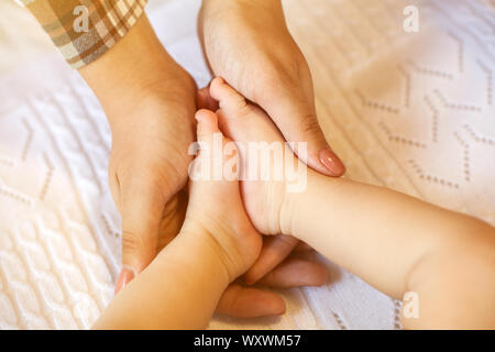 Cute little baby's legs in mother's hands close up in bed at home. Family, maternity and childhood concept. Stock Photo