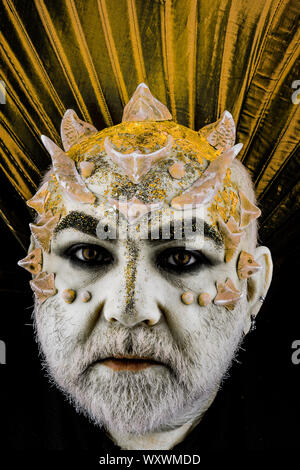 Head with thorns or warts, face covered with glitters, close up. Demon with golden collar, black background. Alien, demon, sorcerer makeup. Fantasy Stock Photo