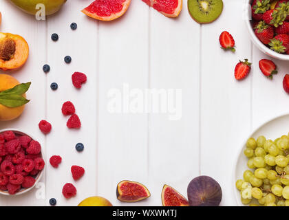 Fruits and berries arranged into frame on the white wooden background Stock Photo