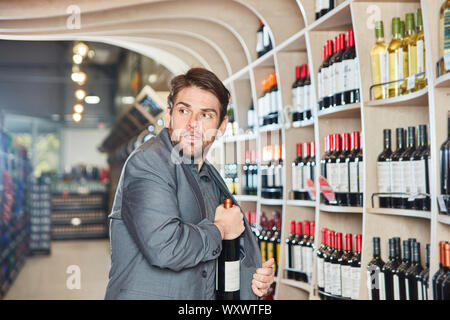 Young man puts a bottle of wine in his jacket during shoplifting Stock Photo