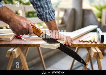 Adult craftsman carpenter with manual saw working on cutting a wooden table. Housework do it yourself. Stock photography. Stock Photo