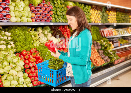 Young woman as customer is holding a fresh paprika while buying vegetables in supermarket Stock Photo