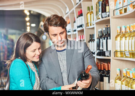 Young couple buying red wine reads label on the bottle in front of the wine rack Stock Photo