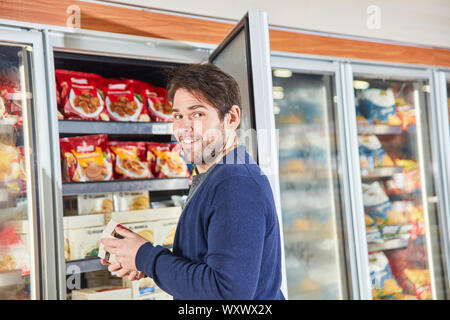 Man as a customer while shopping frozen food in the refrigerated shelf in the supermarket Stock Photo