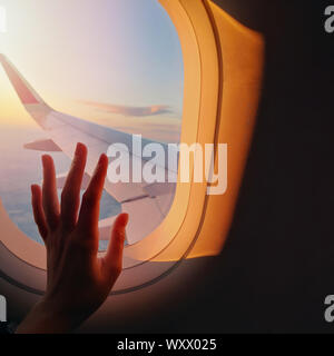 Woman's hand touching a window glass on the plane in sunset light Stock Photo