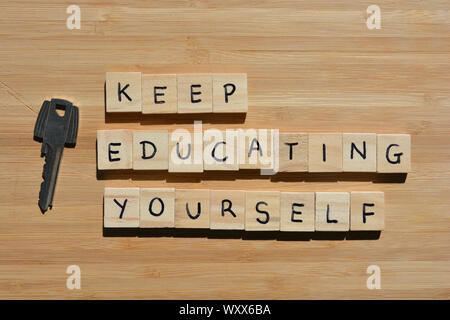 Keep Educating Yourself. Motivational words, using the acronym KEY. Wooden alphabet letters next to a metal key on a wooden background Stock Photo