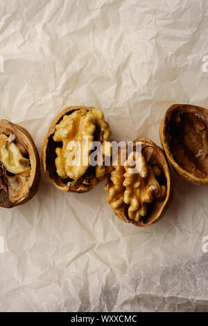 Raw walnuts in cracked nutshells on parchment paper. Overhead view Stock Photo