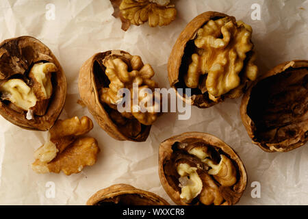 Raw walnuts in cracked nutshells on parchment paper. Overhead view Stock Photo