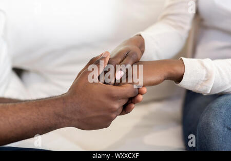 African American Couple Holding Hands While Sitting On Couch Stock Photo