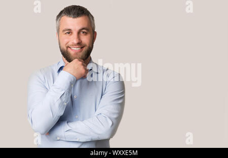 Interested smiling bearded man touching chin over white background Stock Photo