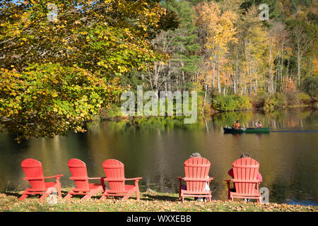 Tourists in Muskoka chairs, also knowns as Adirondack chairs and canoe on Lake Rescue near Ludlow in Vermont, New England, USA Stock Photo