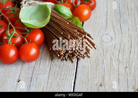 Wholegrain rye spaghetti, tomatoes and herbs on wood Stock Photo