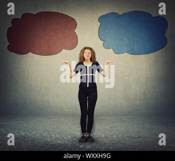 Cheerful teen girl balancing hands, spread arms gesture, giving two options to choose right or left side as holding different colored blank thought bu Stock Photo