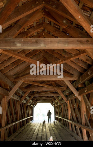 Trusses and beams in geometric shapes and man walking dogs at The Old Covered Bridge, bridge by Sheffield Plain, Massachusetts. Stock Photo