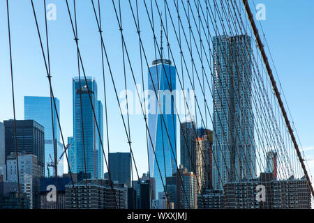 Skyscrapers of Manhattan viewed through wire supports and cables of Brooklyn Bridge, New York City Stock Photo