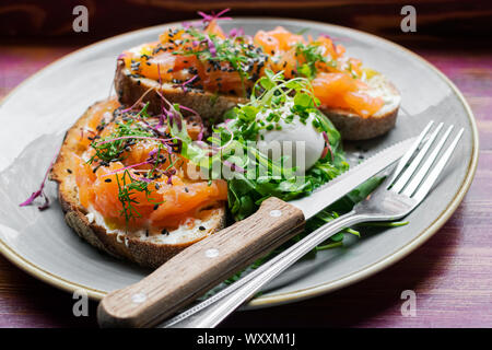 Smoked Salmon and cream cheese on rye toast with a poached egg and leafy greens on a table in the window of a boutique restaurant and cafe Stock Photo