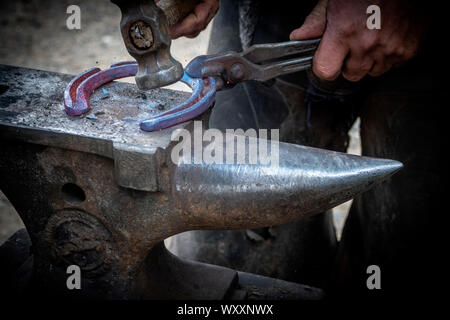 Hand shots of a farrier in the process of shaping a glowing hot shoe on an anvil Stock Photo