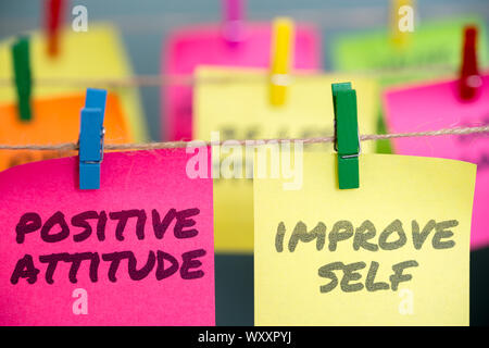 Positive Attitude and Improve Self written in pink and yellow sticky notes are clipped to the rope Stock Photo