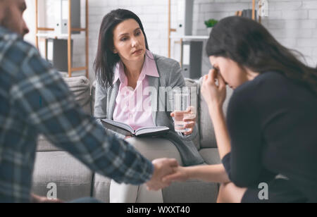 Worried psychologist offering glass of water for woman to calm down Stock Photo