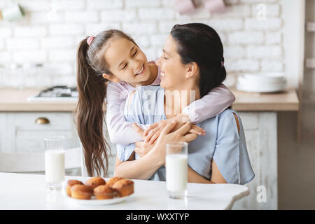 Happy family in kitchen. Daughter cuddling her mother from back Stock Photo