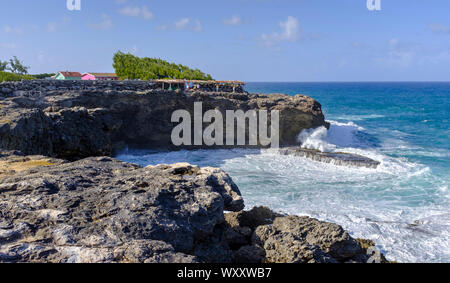 A restaurant and tourist shops perched on a cliff overlooking the ocean waves at North Point, Barbados Stock Photo