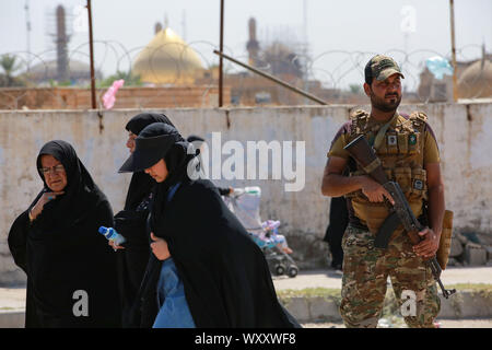 Samarra, Iraq. 18th Sep, 2019. Women walk past a member of the Peace Companies (Saraya al-Salam), an Iraqi armed group linked to Iraq's Shia community and part of the Iraqi state-sponsored Popular Mobilization Forces (PMF), as he stands guard during security precautions against potential threats by the so-called Islamic State (IS) terror group. Credit: Ameer Al Mohammedaw/dpa/Alamy Live News Stock Photo