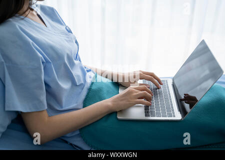 Young asian woman sick patient lying in a hospital bed using a laptop for relax when she recovering for ill in hospital. Stock Photo