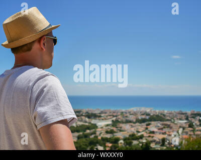 A man in a hat looks in front of him at a beautiful view of a settlement by the sea Stock Photo