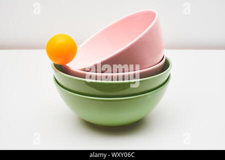 Pink and green earthenware and porcelain bowls, isolated on a white background, on a table or top, with an orange ball balanced on the edge Stock Photo