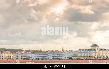A view of the white fronted hotels lining the promenade at Llandudno.  A sky with heavy cloud is above and the beach in the foreground. Stock Photo