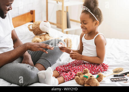 Cheerful black girl making manicure for daddy Stock Photo