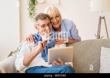 Happy pensioners using tablet, relaxing on rug Stock Photo