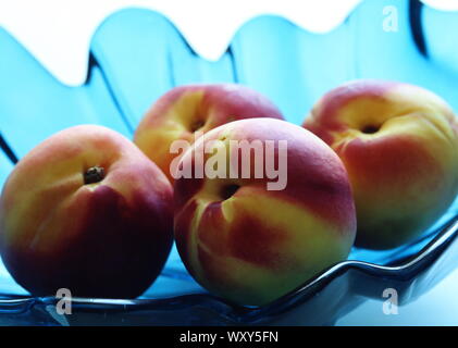 Close up of red and yellow peaches in decorative turquoise blue glass bowl against white background Stock Photo