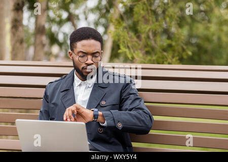 Freelance man working on laptop outdoors and checking time Stock Photo