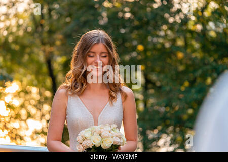 Smiling happy Bride holding Wedding bouquet in hands in front of groom at wedding day outdoors at park. Bride with closed eyes waiting for surprise Stock Photo